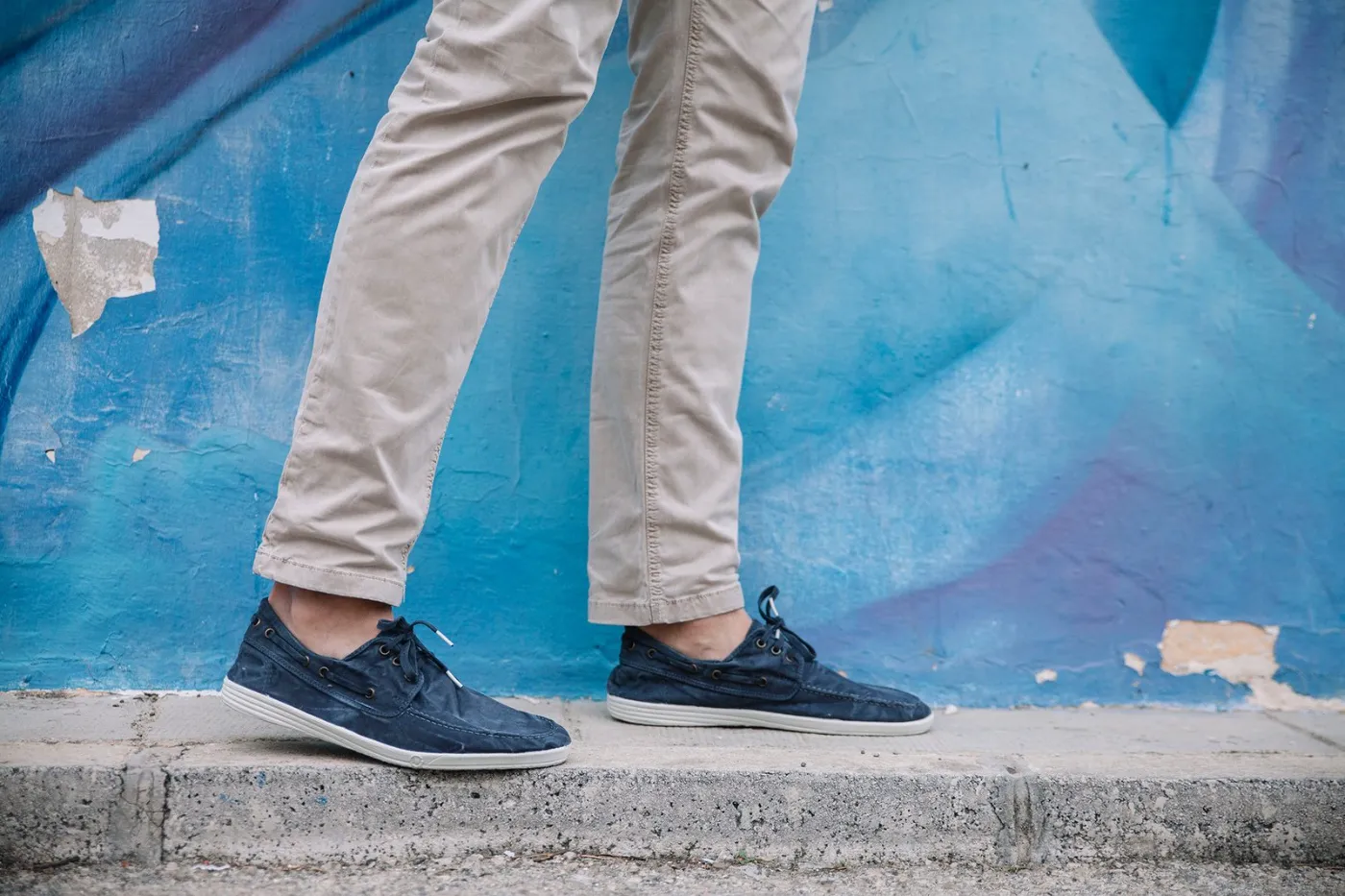 Natural World navy sneakers against a blue wall